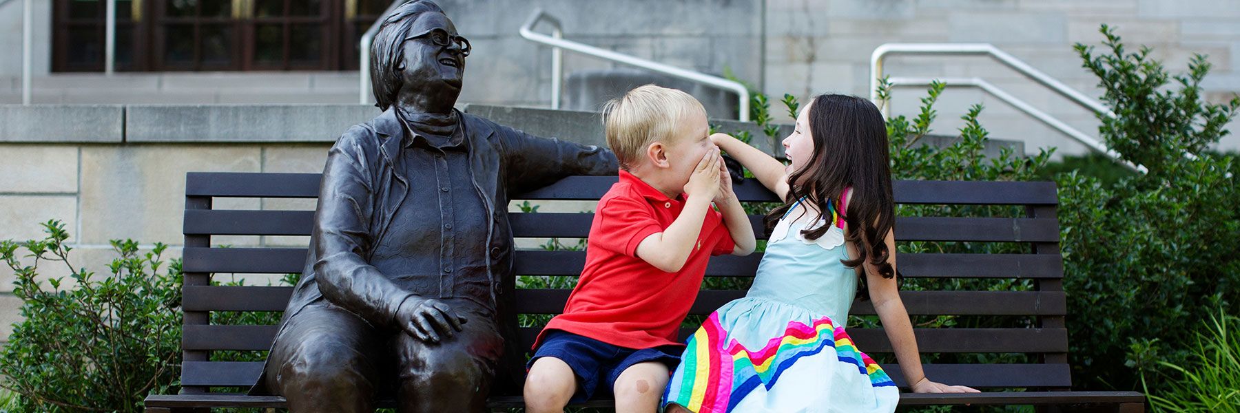 Two children laughing and sitting on a bench with a statue of IU professor Elinor Ostrom.